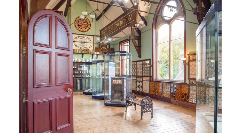 A burgundy door open to reveal a former showroom displaying colourful tiles.